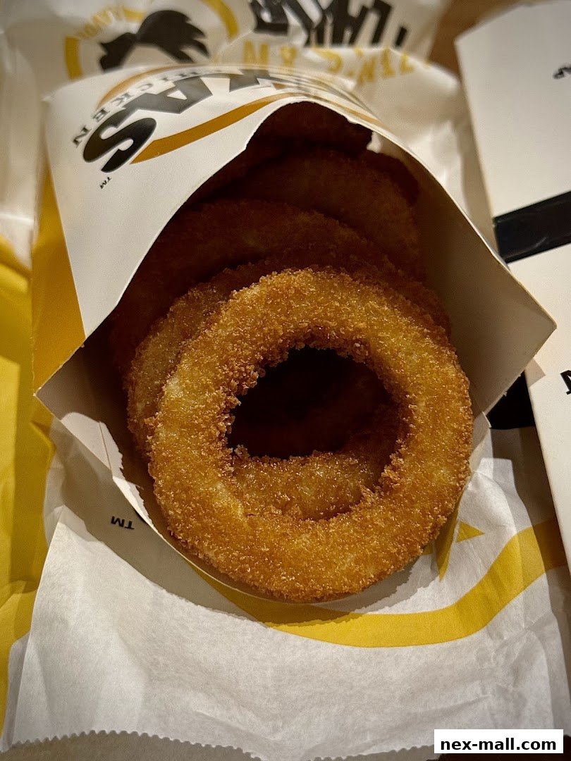 A close-up shot of crispy, golden onion rings served in a branded paper container.