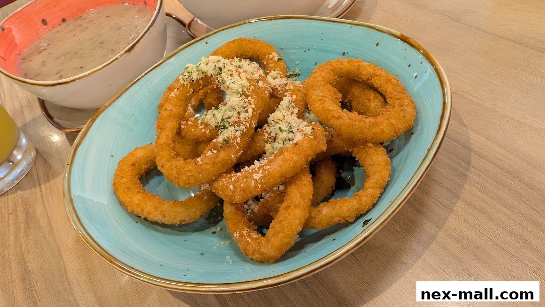 A plate of crispy onion rings with grated cheese and a bowl of soup in the background.