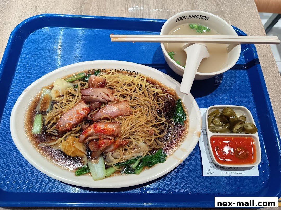 A plate of dry noodles with char siu, wontons, vegetables, and a side of soup and chili.