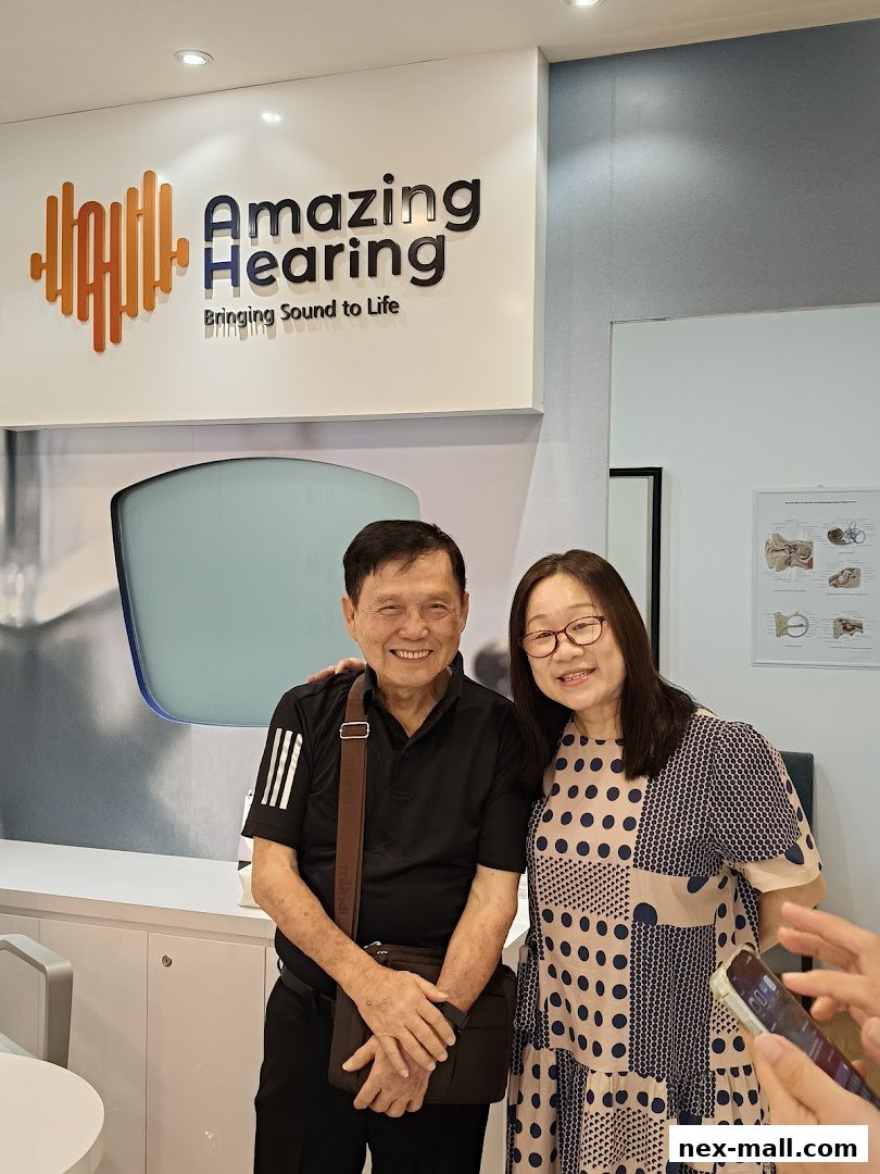 A man and a woman smiling in front of the Amazing Hearing shop logo.