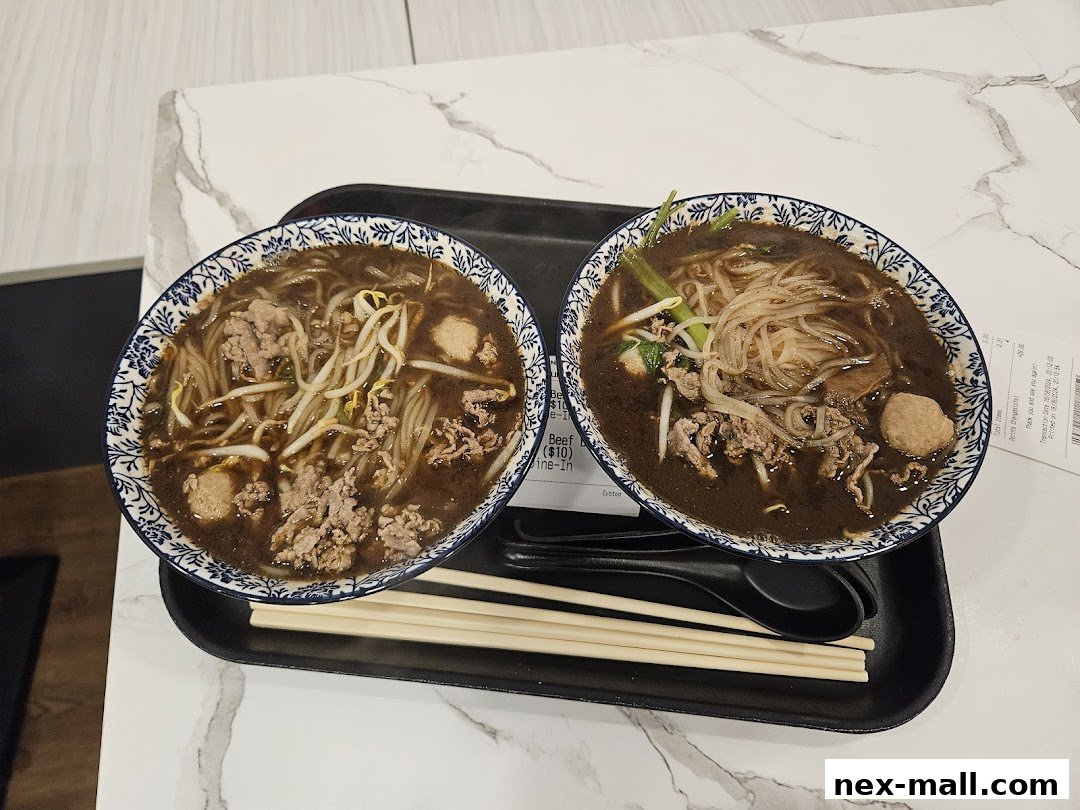 Two bowls of steaming beef noodle soup served with chopsticks and spoons on a tray.