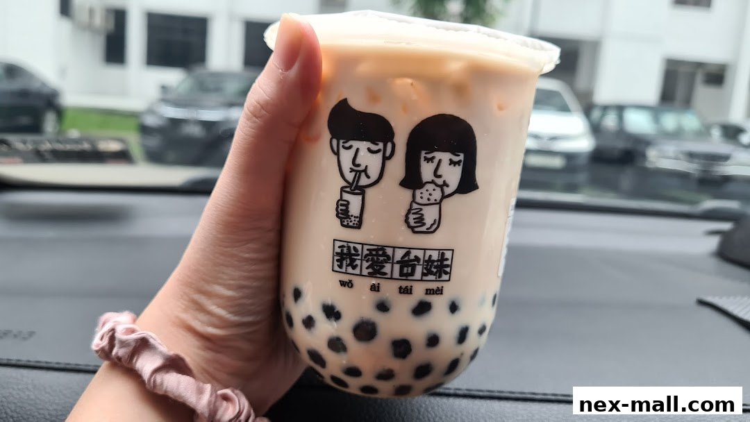 A hand holds a bubble tea cup with the shop's logo and text.