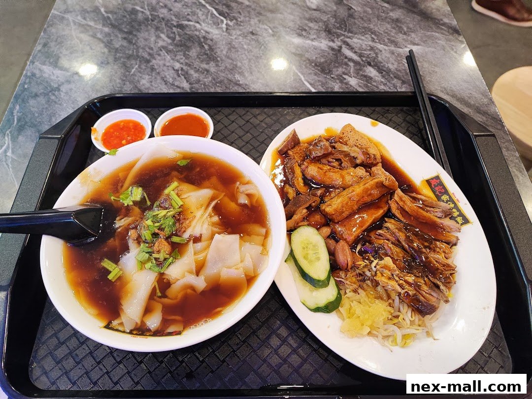 A bowl of noodle soup and a plate of roasted duck with side dishes on a tray.