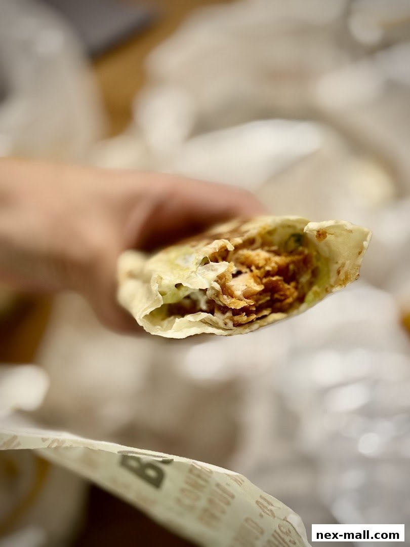 A hand holds a delicious chicken wrap, showcasing the tender chicken and fresh ingredients.