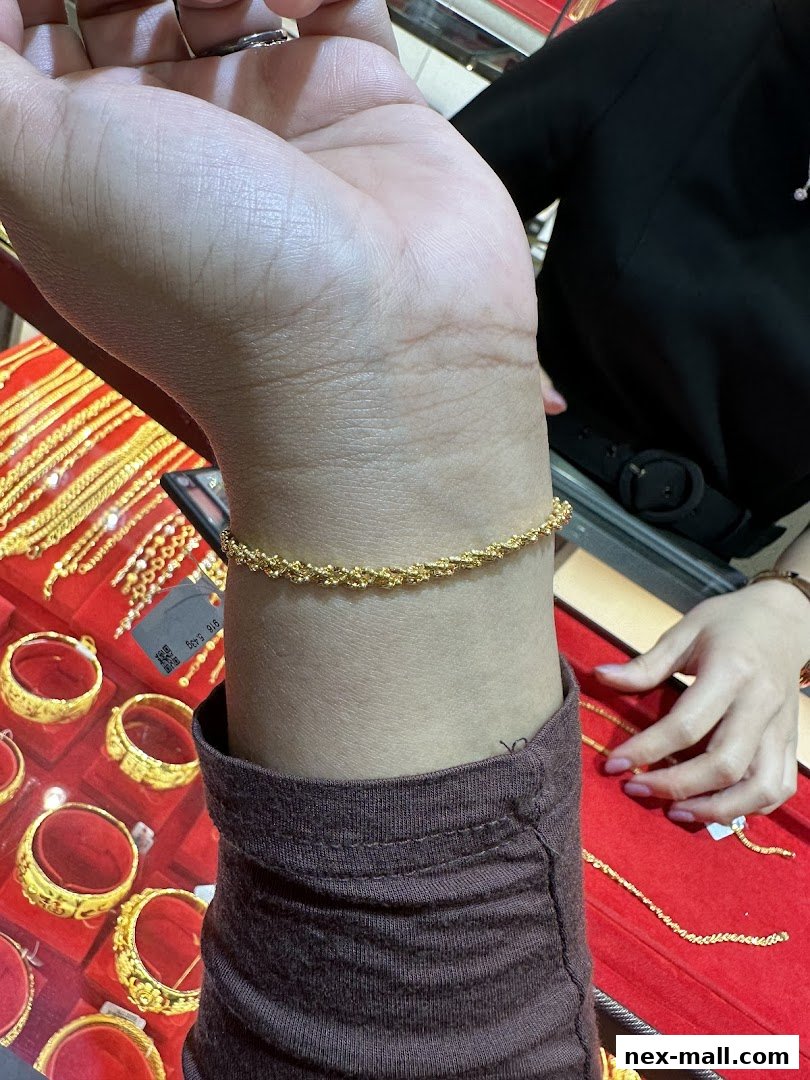 A person tries on a delicate gold bracelet in a jewelry store with display cases of gold jewelry.