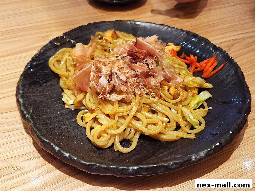 A close-up of a plate of yakisoba noodles topped with bonito flakes and shredded carrots.