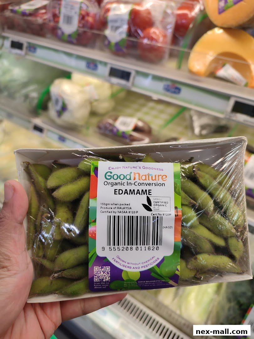 A hand holds a package of Good Nature Organic In-Conversion Edamame in a supermarket aisle.