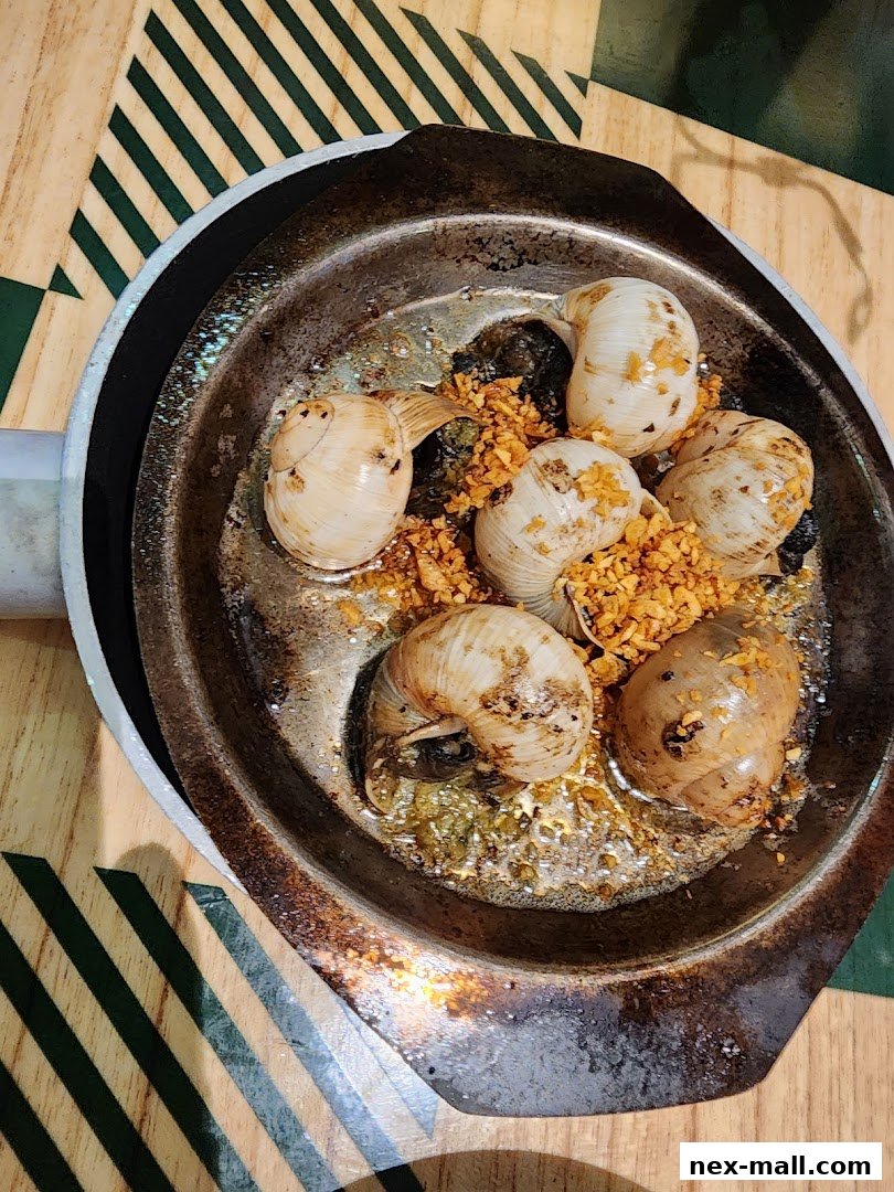 A close-up shot of escargots cooked in garlic butter and served in a metal dish.
