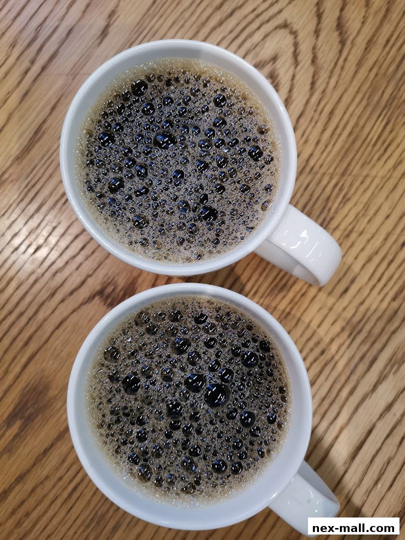Two white mugs filled with freshly brewed coffee sit on a wooden table.