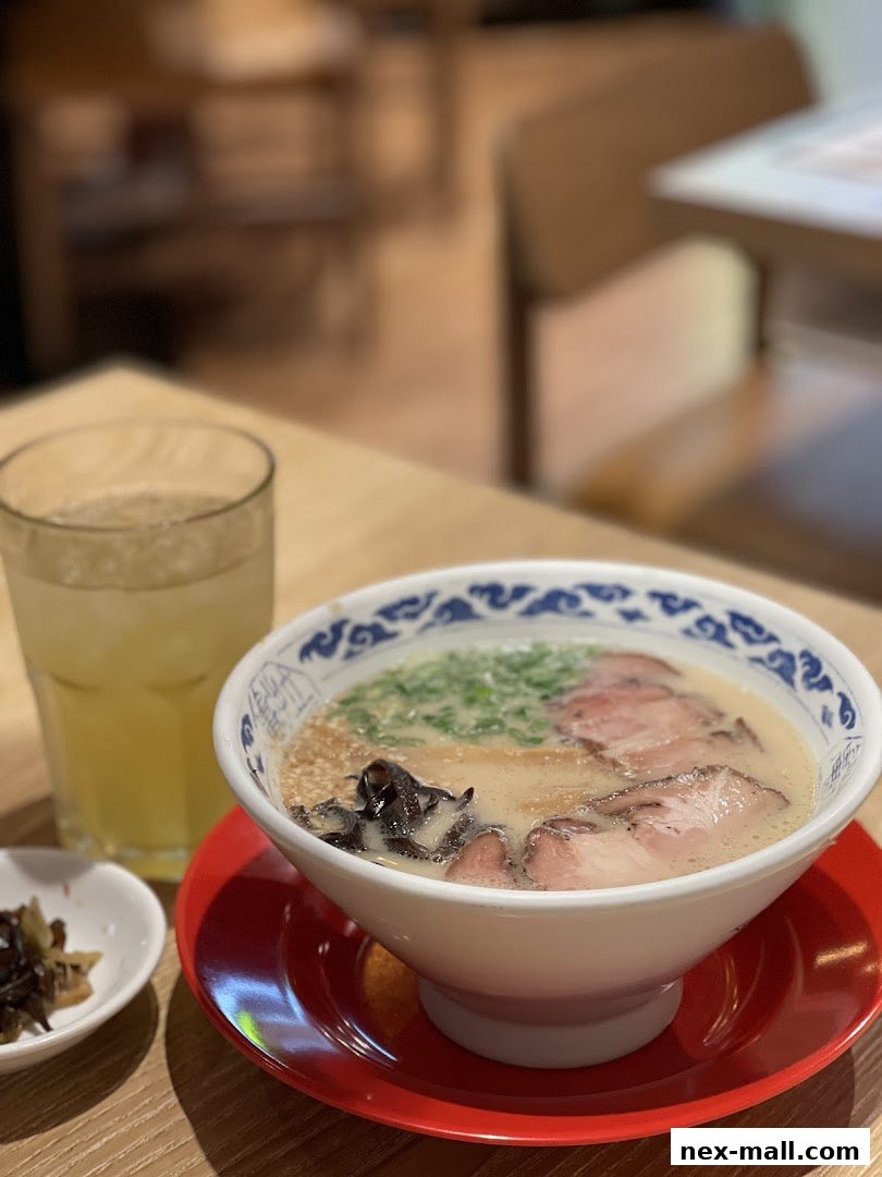 A steaming bowl of ramen with pork slices, green onions, and a side of pickled vegetables.