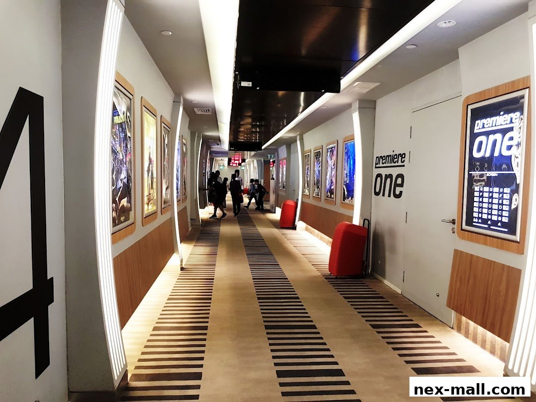 A cinema hallway with movie posters, illuminated walls, and people walking.