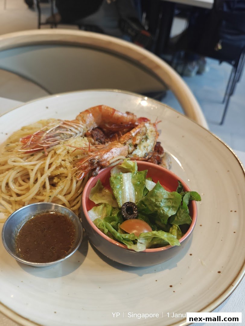 A plate of spaghetti with prawns and a side salad, served at a restaurant.