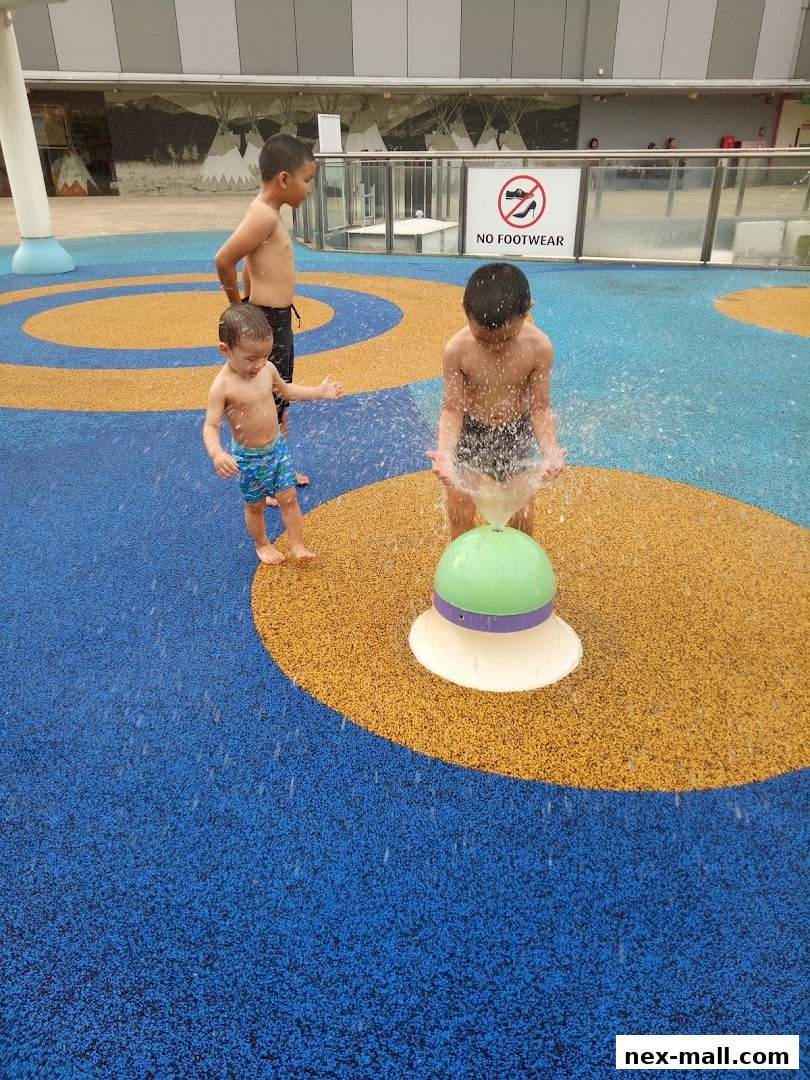 Three boys playing in a water play area with colorful ground and a water feature.
