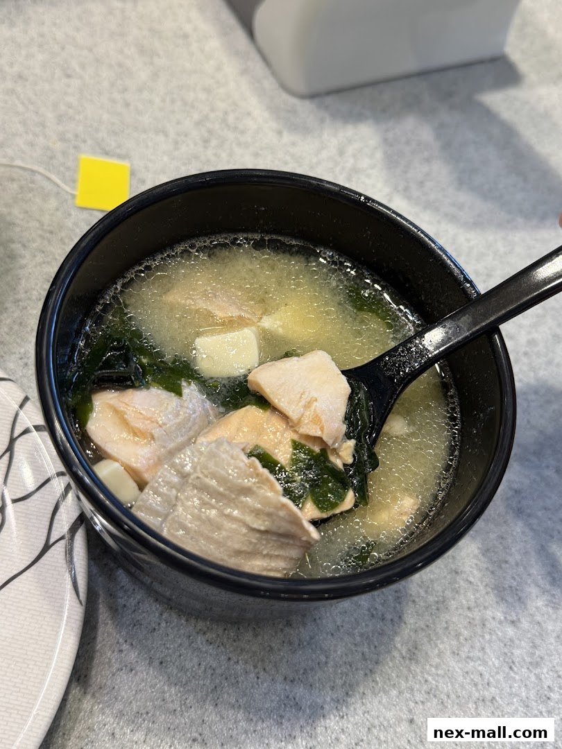 A close-up shot of a bowl of miso soup with salmon, tofu, and seaweed.