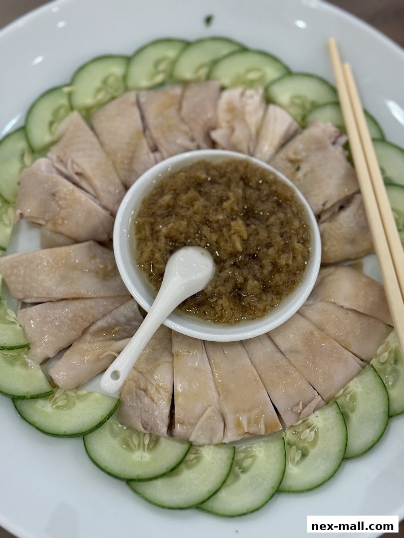 A plate of sliced chicken with cucumber slices and a bowl of dipping sauce.