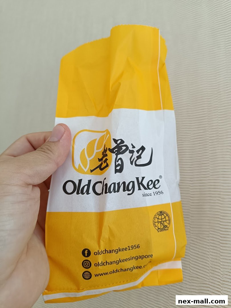 A hand holds a yellow and white paper bag with the Old Chang Kee logo and social media handles.