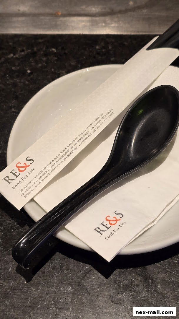 A close-up of a Japanese restaurant's table setting with chopsticks, a spoon, and branded napkins.