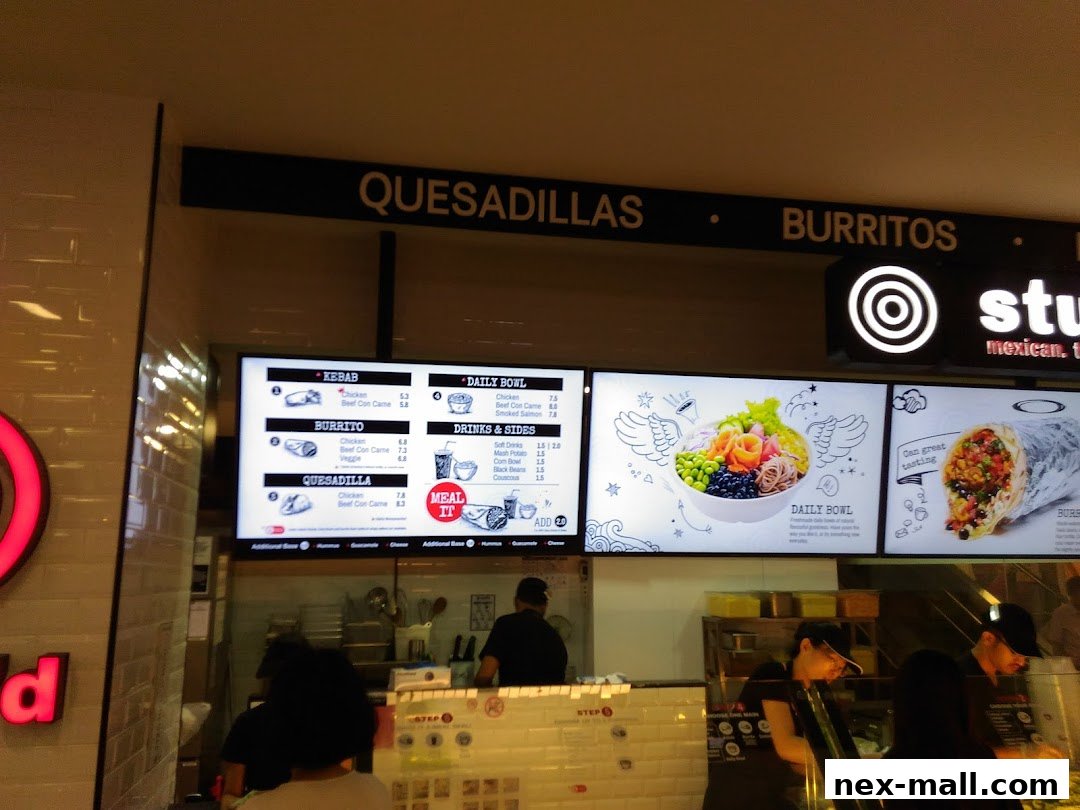 A view of the Stuffd shop counter with digital menus displaying food items and staff serving customers.