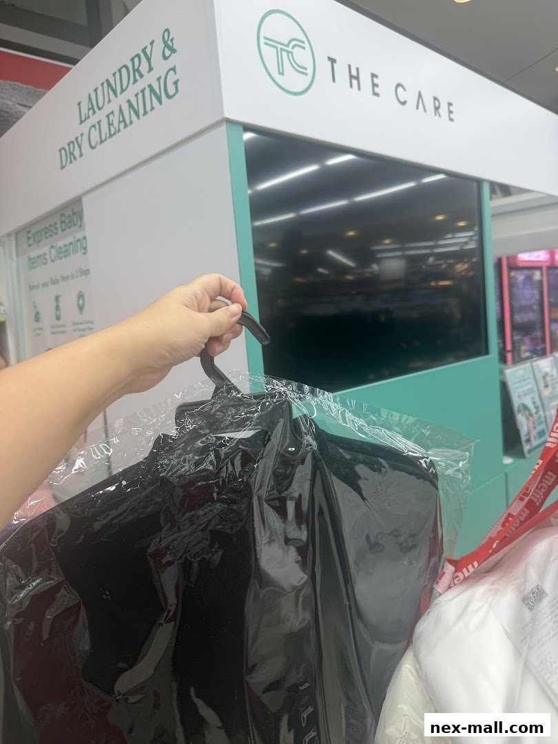 A hand holds a black garment on a hanger, in front of a laundry and dry cleaning shop.