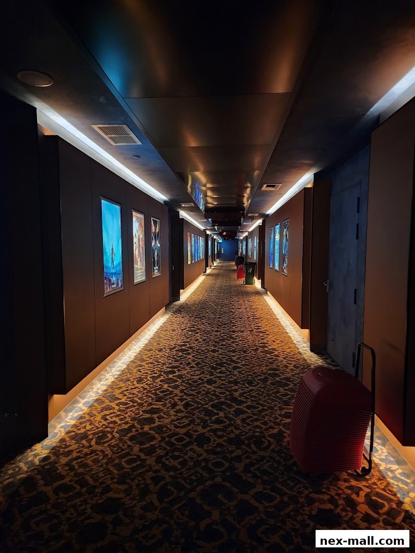 A dimly lit cinema hallway with movie posters and a red luggage cart.
