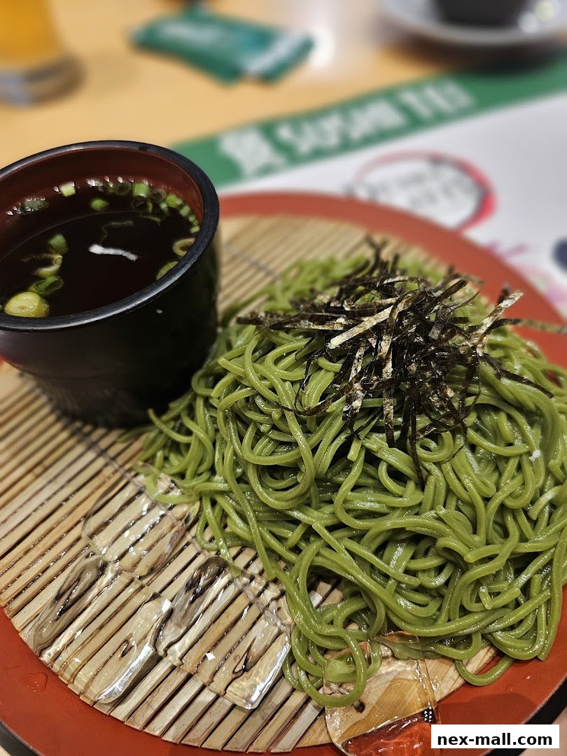 A close-up of green soba noodles with seaweed and a dipping sauce.