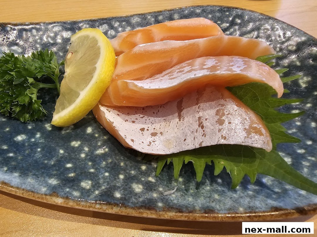 A plate of fresh salmon sashimi with a lemon slice and parsley garnish.