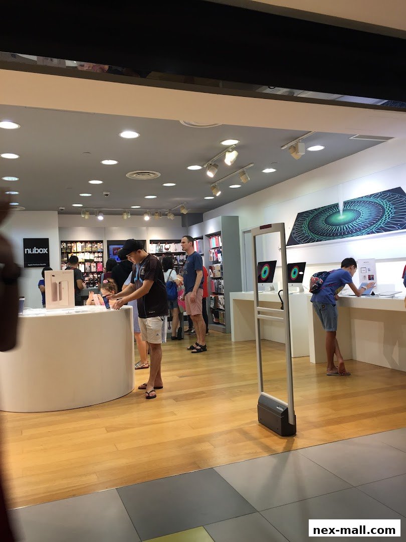 Customers browse Apple products inside a modern electronics store with bright lighting.