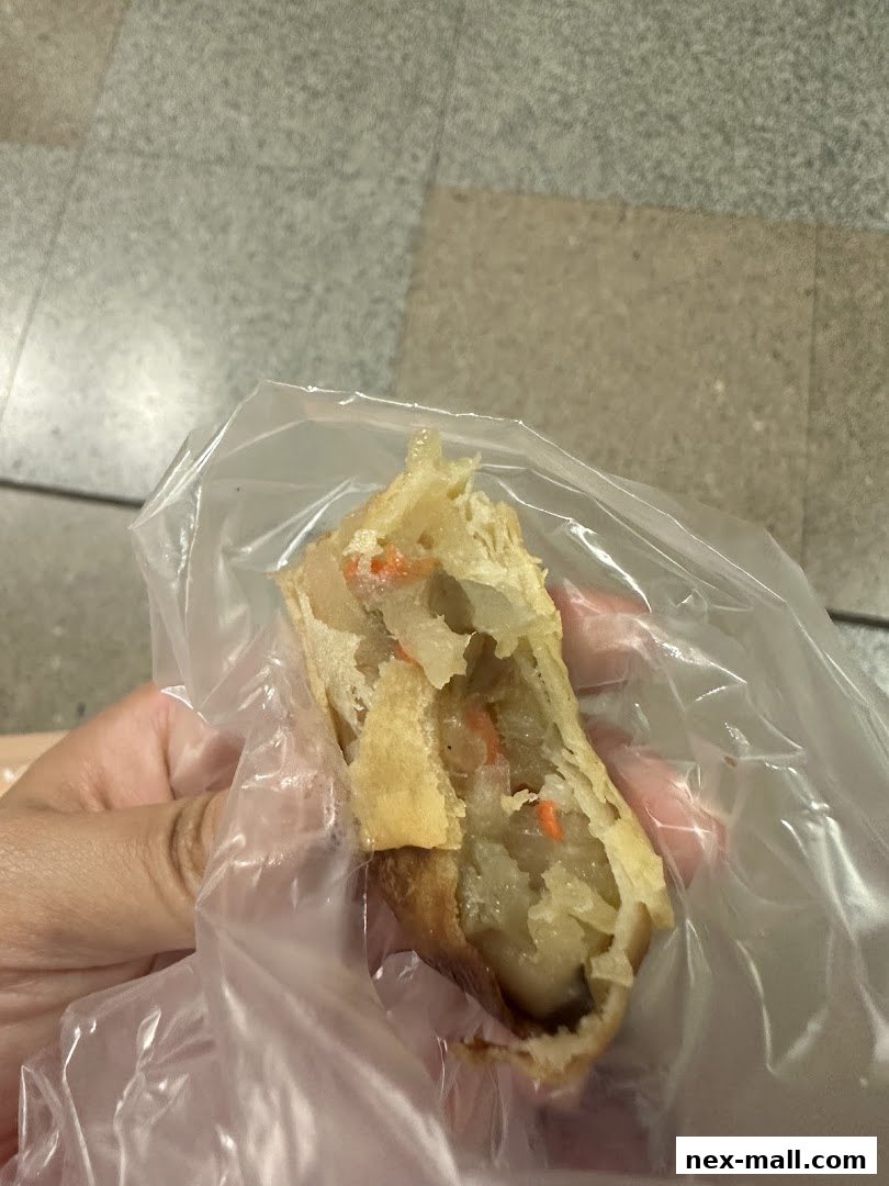A hand holds a half-eaten savory pastry filled with vegetables in a plastic bag.