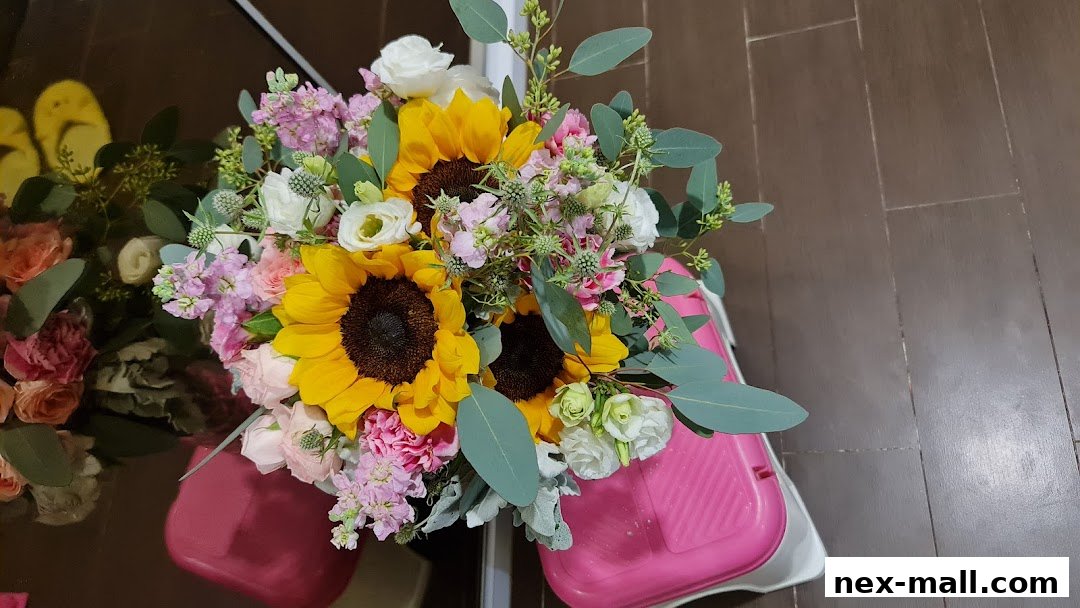 A vibrant bouquet of sunflowers, roses, and other flowers in a pink container.