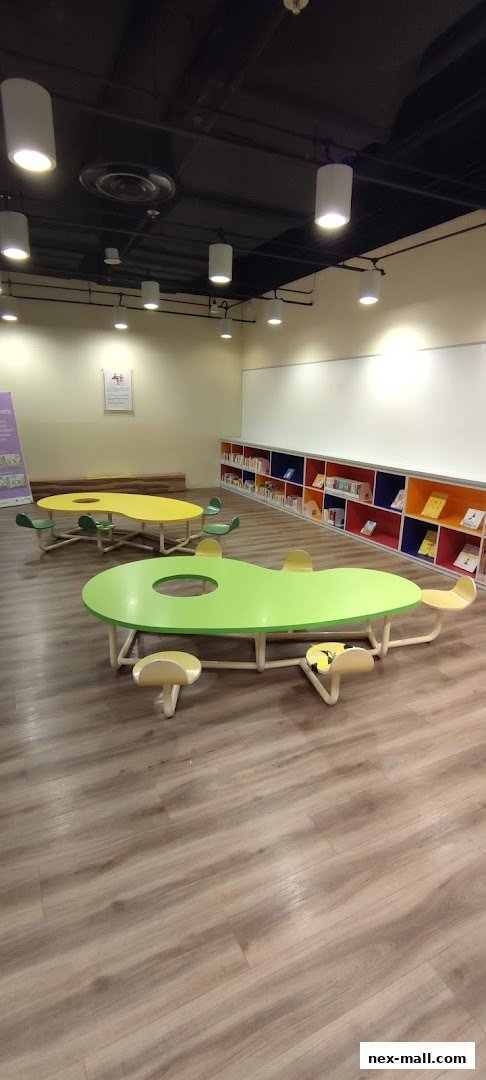 A brightly lit children's reading area with colorful tables and chairs, and bookshelves.