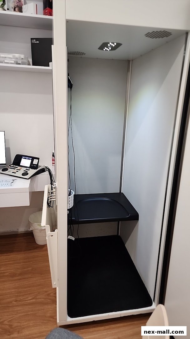 Interior view of a sound booth with testing equipment and shelves in a hearing clinic.