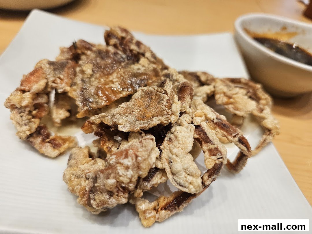 Crispy fried soft shell crab served on a white plate with a dipping sauce.