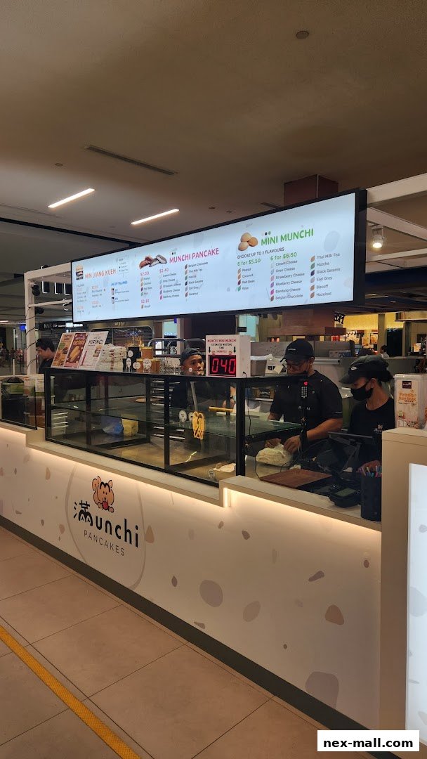 A brightly lit pancake shop counter with staff preparing food and a menu board above.