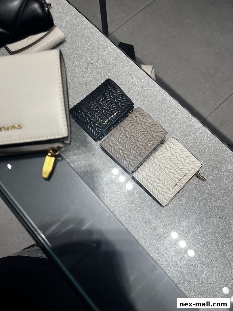 A display of Charles & Keith wallets in black, grey, and white with textured designs.
