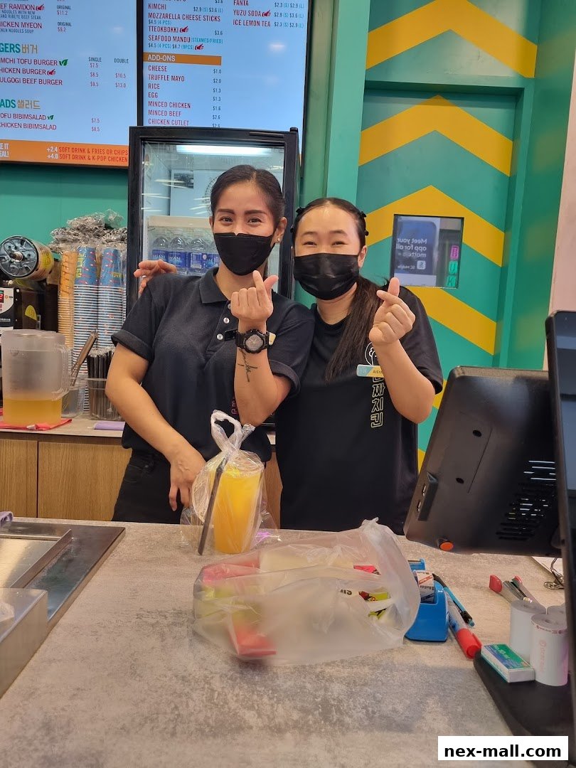 Two smiling staff members at JINJJA Chicken NEX, making finger hearts.