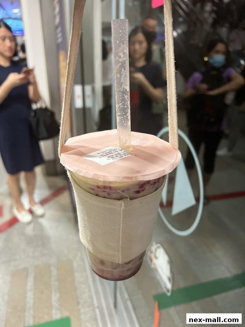 A person holds a drink with a straw and a fabric sleeve, with blurred people in the background.
