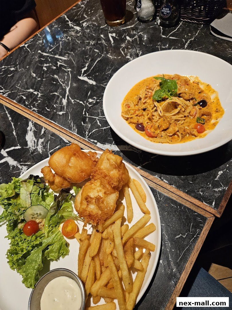 A table setting with two plates of food: fish and chips with salad, and a pasta dish.