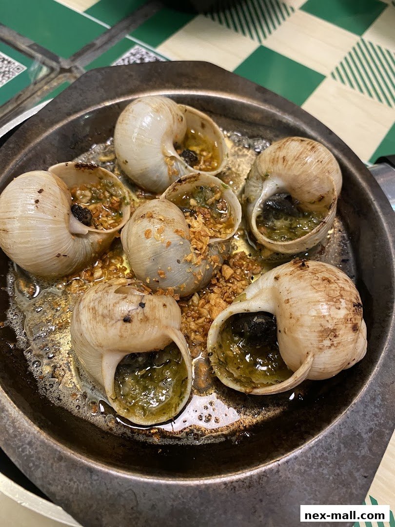 A close-up shot of escargots cooked in garlic butter and herbs, served in a metal dish.