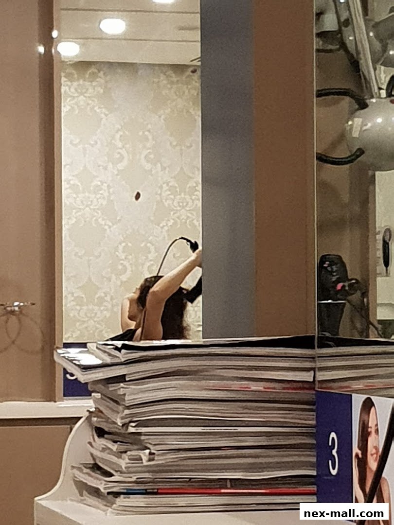 A woman's reflection in a mirror, with a stack of magazines in the foreground.