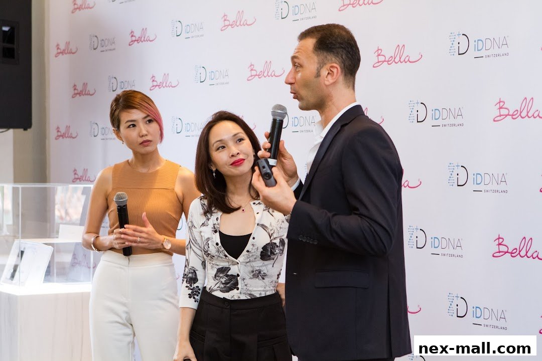 Three people stand in front of a branded backdrop, two women and one man holding microphones.
