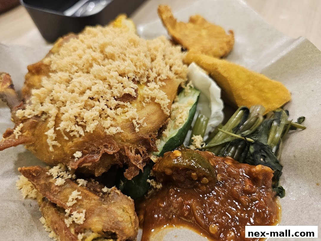 A close-up of a delicious Ayam Penyet dish with crispy fried chicken, vegetables, and sambal.