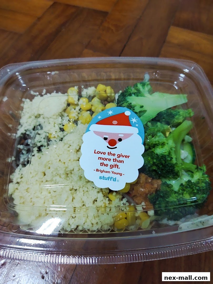 A clear plastic container filled with a healthy meal of couscous, corn, and broccoli, topped with a festive Santa sticker.