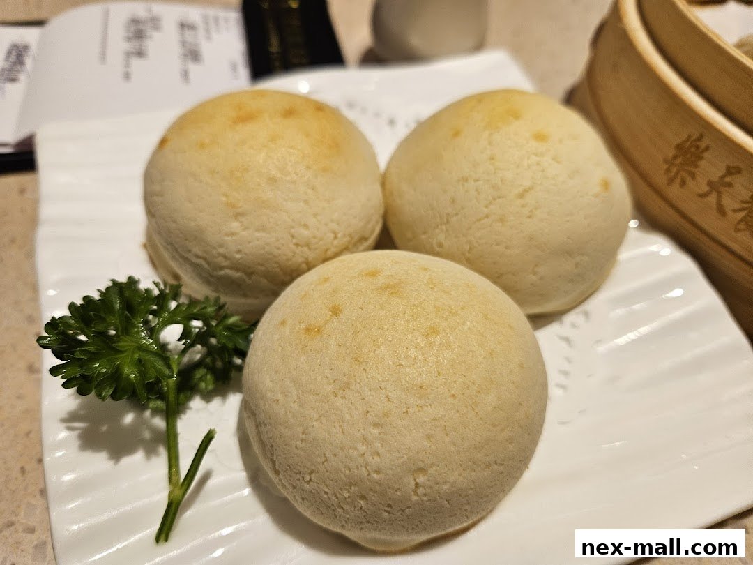 Three golden-brown baked buns served on a white plate with a sprig of parsley.