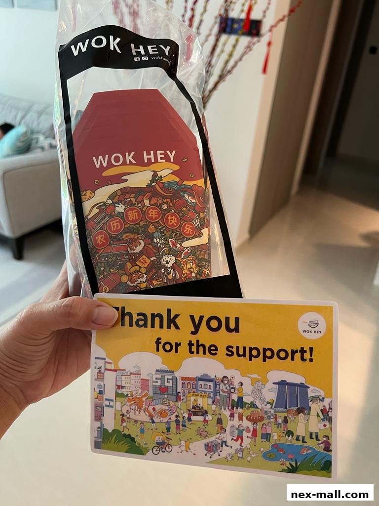 A person holds a Wok Hey bag with red packets and a thank you card.