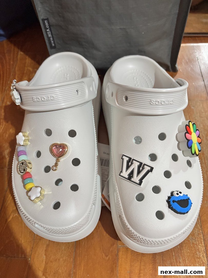 A pair of white Crocs adorned with colorful Jibbitz charms and letter patches.