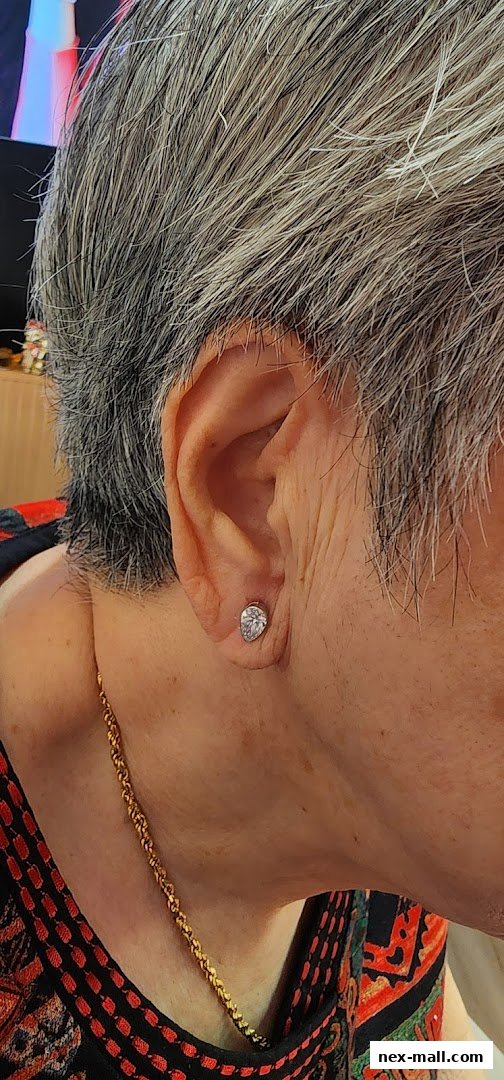 Close-up of a person's ear wearing a diamond stud earring and a gold chain necklace.