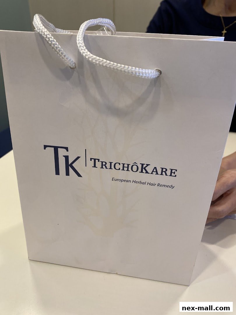 A white paper bag with the TK Trichokare logo and 'European Herbal Hair Remedy' text.