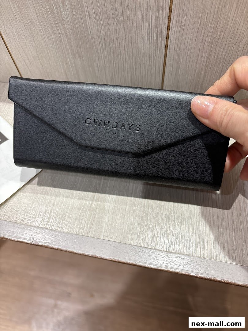 A black OWNDAYS glasses case held by a hand against a wooden background.