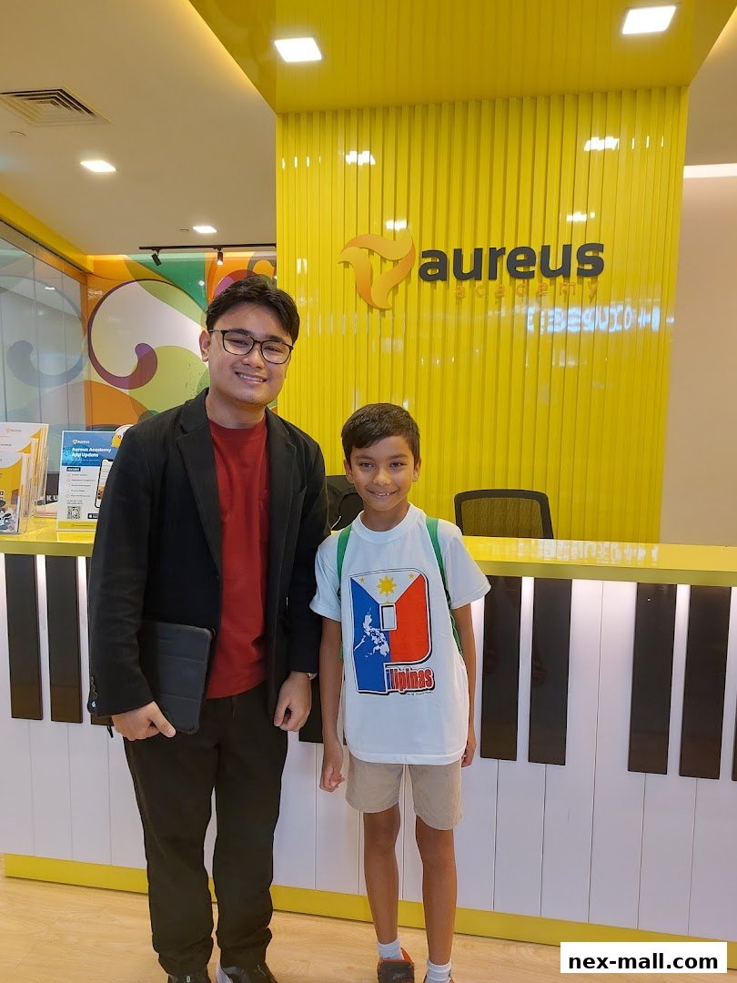 Two smiling individuals stand in front of the Aureus Academy reception desk with a piano-themed counter.