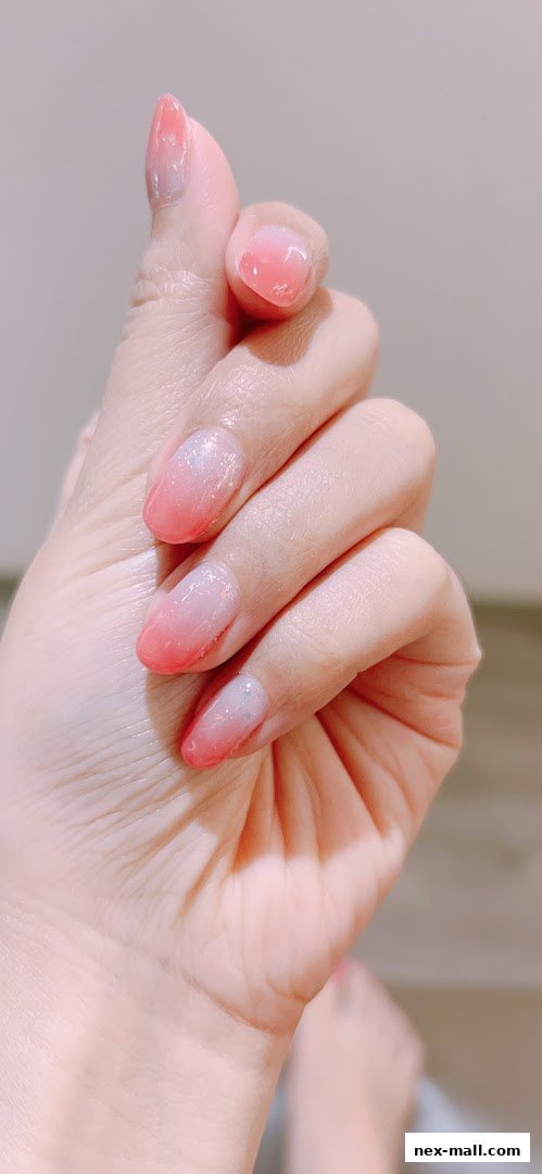 A close-up shot of a hand with beautifully manicured nails featuring a pink and white ombre design with glitter.